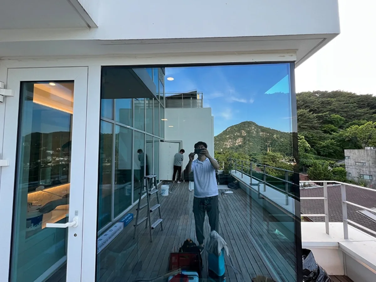 목재 데크 테라스에서 작업자가 사다리를 두고 통유리 시공을 준비하는 사진