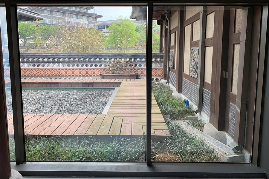 필름 시공 전 실내에서 바깥 마당과 조경이 그대로 비치는 한옥 양식 전시관 통유리 사진