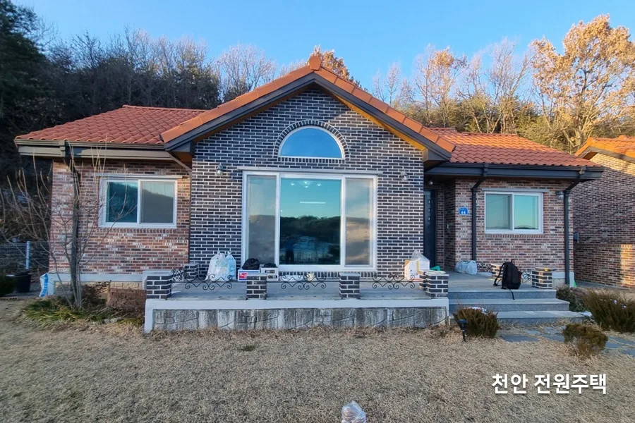 붉은 기와지붕과 벽돌 외벽의 전원주택 전경, 마당에 나무가 있는 사진