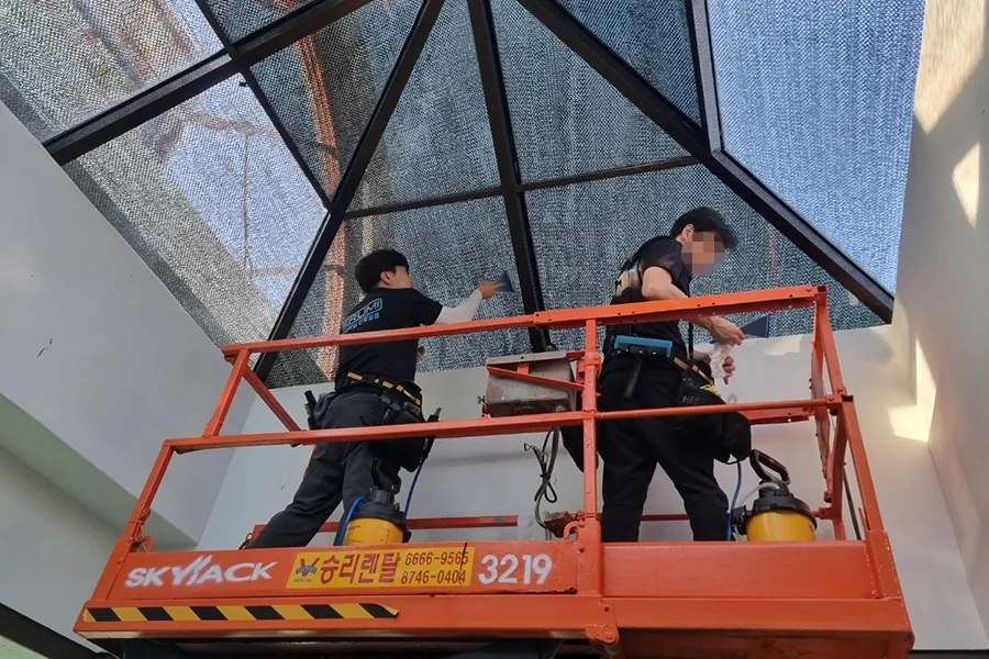 고소작업대에 올라 각진 유리 지붕을 시공하는 작업자 두 명의 사진