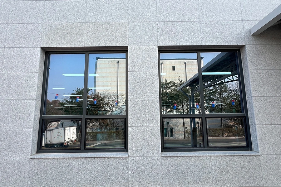 건물 외부에서 바라본 시공 후 창문, 유리에 옅은 톤이 고르게 적용되어 주변 건물이 반사되는 사진