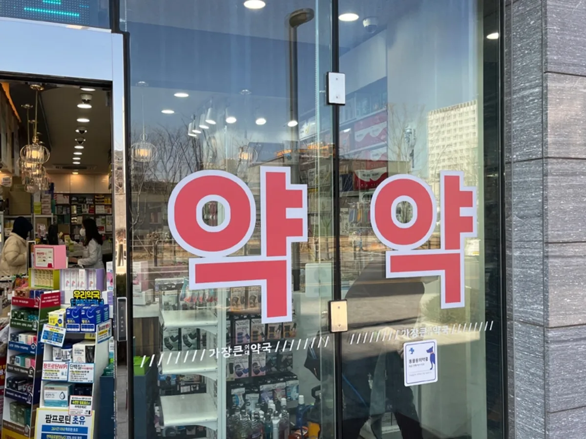 약국 출입문 유리에 안내 스티커가 여러 겹 부착된 시공 전 사진