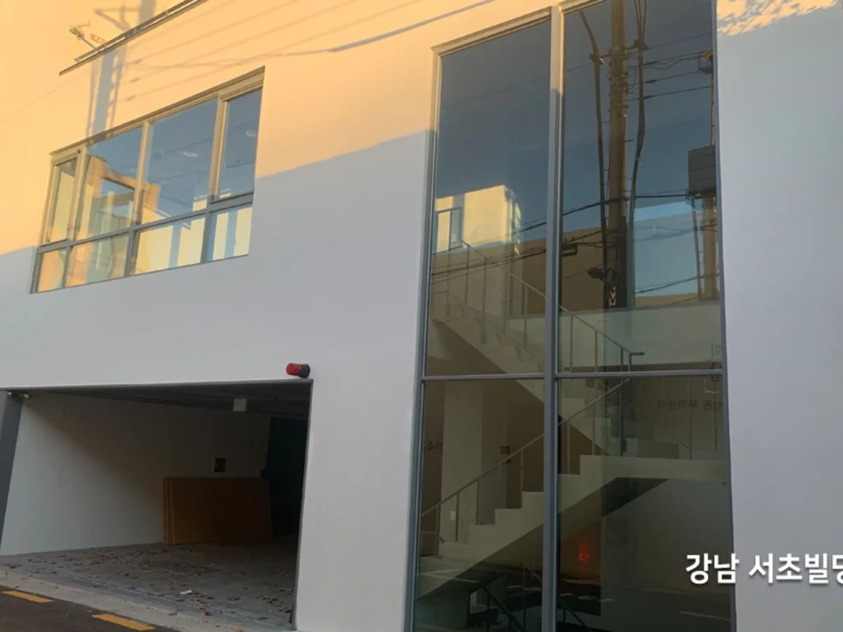 사옥 1층 출입구 옆 세로로 긴 통유리와 주차 공간이 보이는 시공 전 사진