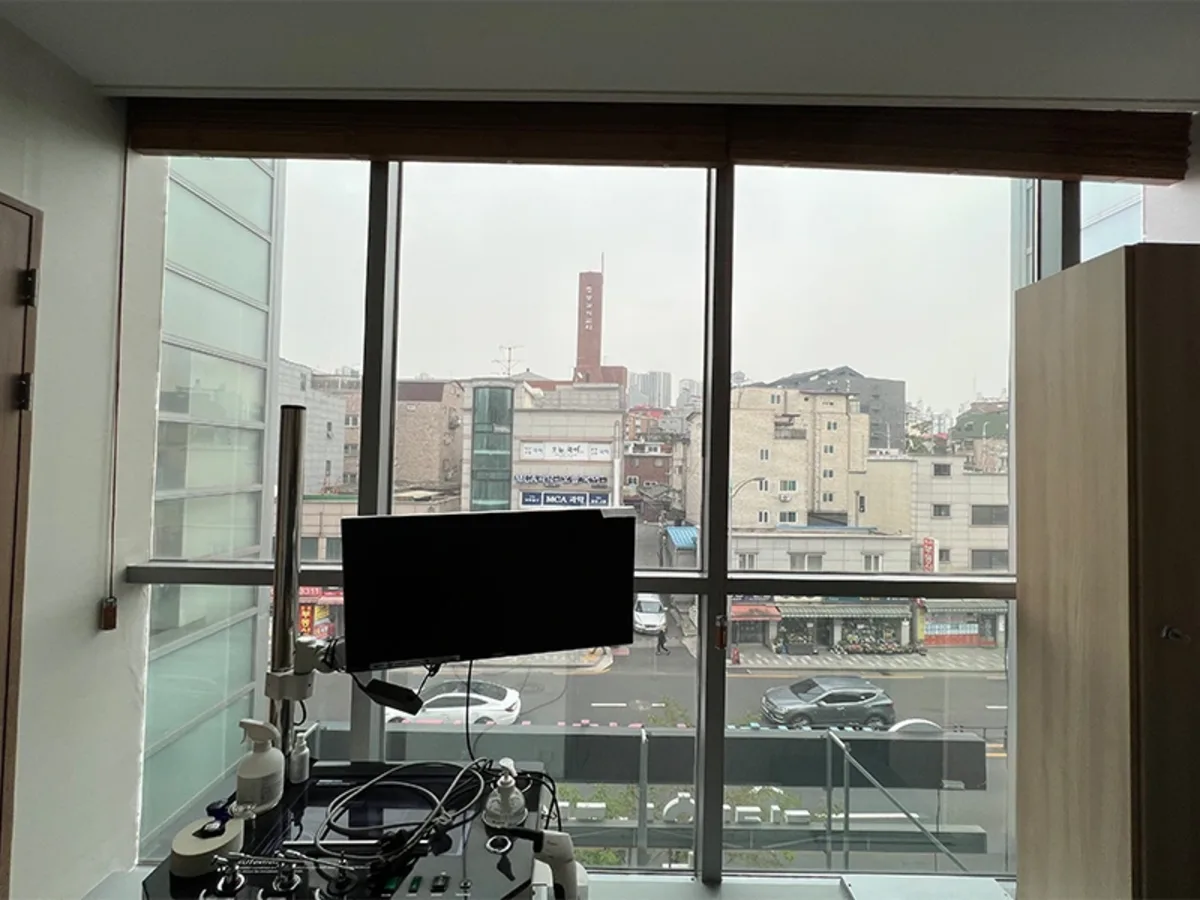진료실 창가에 모니터와 의료 장비가 놓여 있고 창밖으로 도심 전경이 보이는 사진