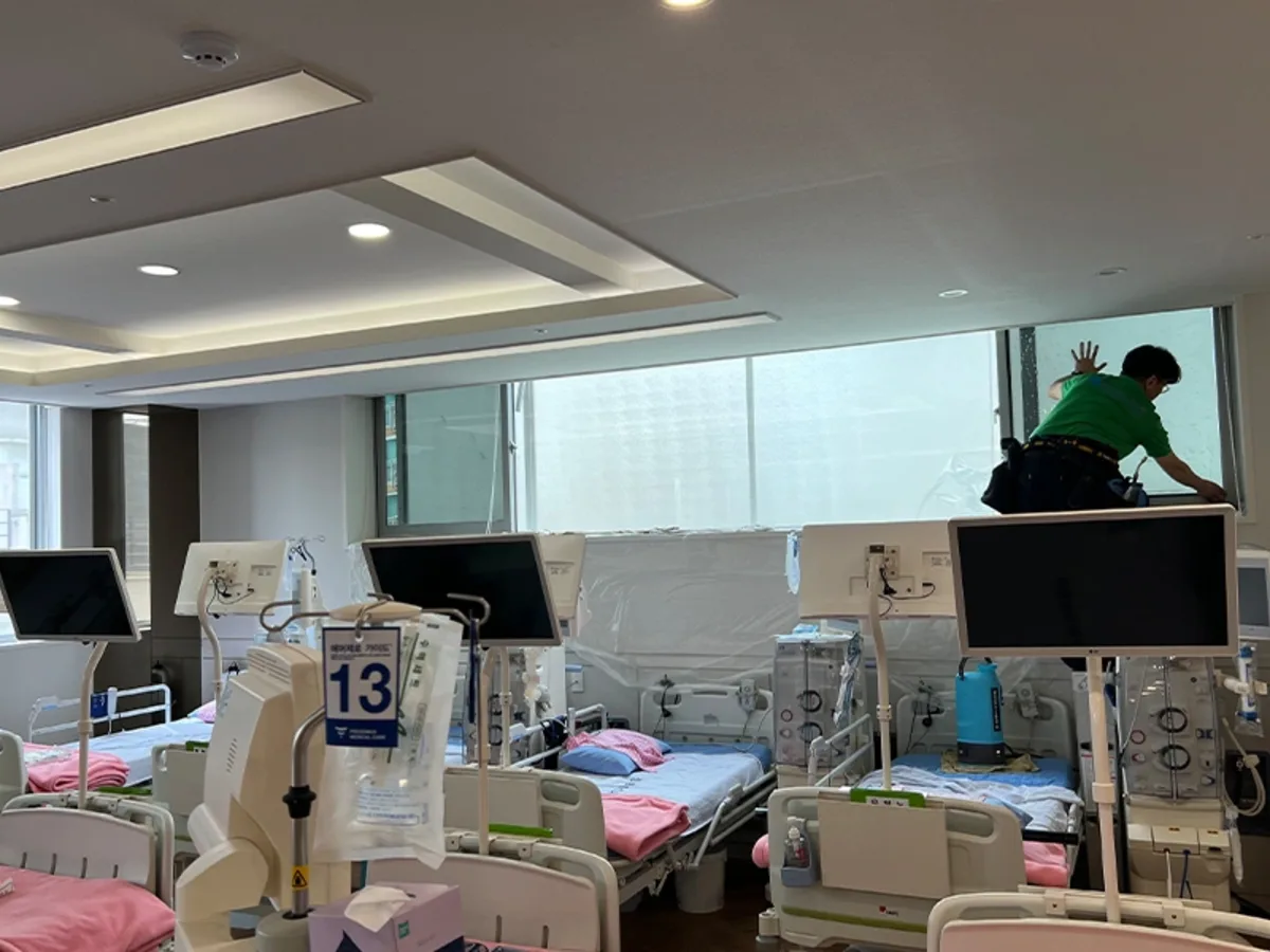 병동 창가에서 작업자가 침상 위 비닐 보양을 마친 뒤 필름을 시공하는 사진